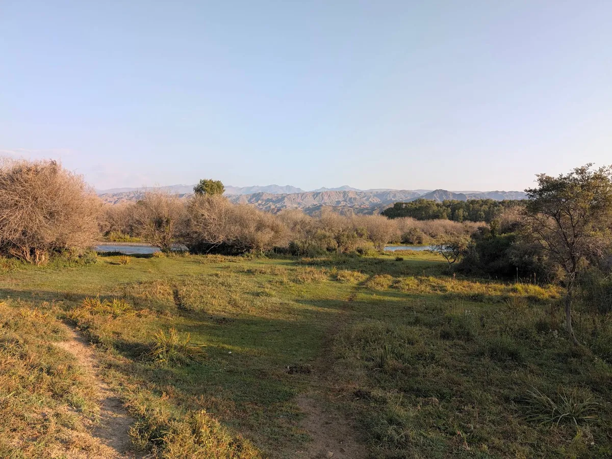 A footpath across the meadow to the river, with mountains on the horizon
